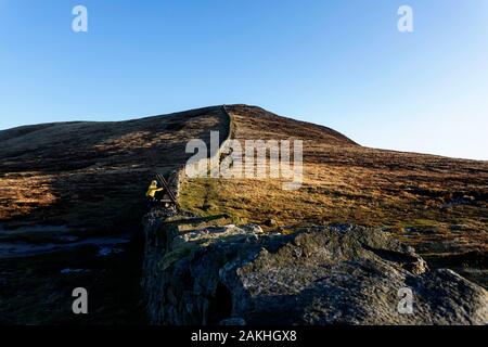 Mourne Mountains und Seen in Nordirland, Großbritannien. Blick vom Gipfel des Slieve Loughshannagh, kleiner Junge, der auf der Holztreppe über die Wand klettert Stockfoto