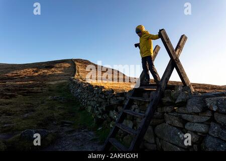 Mourne Mountains und Seen in Nordirland, Großbritannien. Blick vom Gipfel des Slieve Loughshannagh, kleiner Junge, der auf der Holztreppe über die Wand klettert Stockfoto