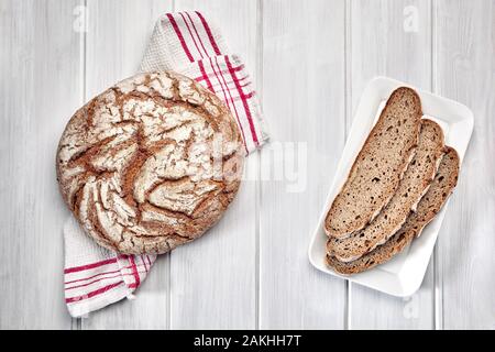 Laib Schwarzbrot und drei Schichten auf einem weißen Holz- Hintergrund. Stockfoto