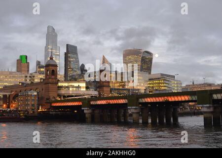 Skyline von London City und Eisenbahnbrücke Cannon Street im nassen Winter am späten Nachmittag mit Mond und Lichtern in Büroblöcken. Stockfoto