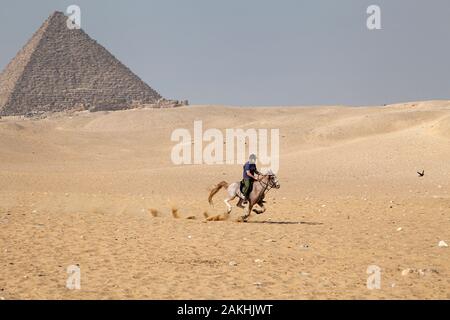 Ein Mann reitet auf einem Pferd durch die Wüste Sand auf Gizeh Plateau in der Nähe der Pyramiden von Ägypten Stockfoto