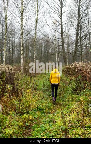 Frau in der hellen Jacke, die den Fallweg in Weißrussland hinunter geht Stockfoto