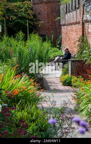 Ein Mann, der in der Kontemplation auf einer Bank in der üppigen Bischof Palace Gardens in der historischen Altstadt von Chichester, West Sussex. Stockfoto