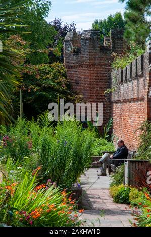 Ein Mann, der in der Kontemplation auf einer Bank in der üppigen Bischof Palace Gardens in der historischen Altstadt von Chichester, West Sussex. Stockfoto