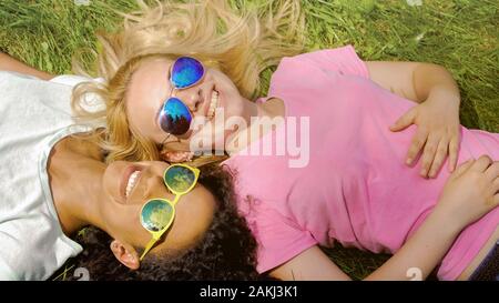 Zwei weibliche Freunde liegen auf Gras im Park, genießen Sommer Wochenende, Freundschaft Stockfoto