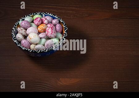 Eine blaue Tasse mit einem Muster ist mit bunten Zucker Dragees gefüllt. Süßigkeiten sind hell hervorgehoben. Braun Holz- Hintergrund. Stockfoto