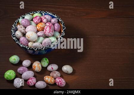 Eine hell erleuchtete blaue Tasse mit einem Muster steht auf einem braunen Holz- Hintergrund. Im Cup und in der Nähe sind bunt süß Dragees. Stockfoto