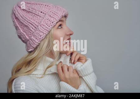 Hübsche junge blonde Frau in der kammgarn winter Outfit kuscheln in die Wärme ihres rollkragen pullover mit einem glücklichen Lächeln, während ein rosa gestrickt tragen kann Stockfoto