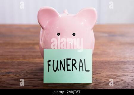 Beerdigung Plan auf einem selbstklebenden Hinweis in der Nähe von Rosa Sparschwein über strukturierte Holzoberfläche geschrieben Stockfoto