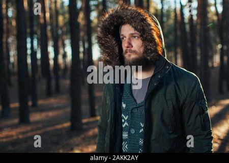 Porträt, Nahaufnahme der Jungen stilvoll ernster Mann mit Bart in rgreen Winter Jacke mit Kapuze und Fell auf dem Kopf bekleidet steht gegen die Rückseite Stockfoto