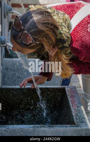 Chestnut Frau trinkt Wasser aus dem Auslauf eines Brunnens Stockfoto