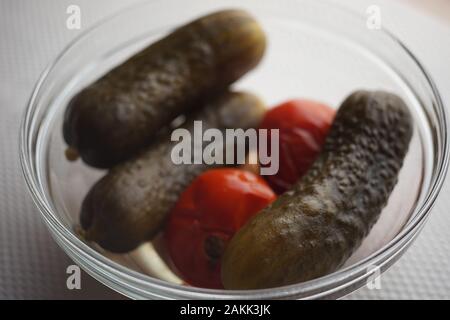 Eingelegte Gurken und Tomaten, Runde Glasschale auf den weissen Tisch, Dosengemüse. Stockfoto