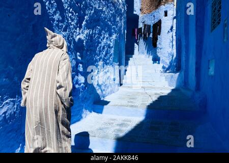 Ein Mann, der gestreifte Djellaba mit Kapuze trägt, die den Kopf des Mannes bedeckt, Medina von Chefchaouen (auch Chaouen genannt), Marokko Stockfoto