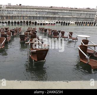 Stühle und Tische im Wasser beim Hochwasser in Venedig in Italien und der antike Palast im Hintergrund Stockfoto