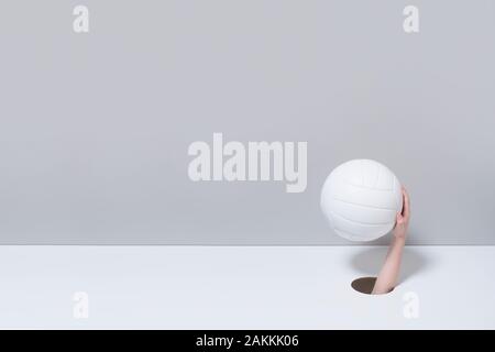 Hand in das Loch. Ein kind Hand hält eine weiße volleyball Ball auf grauem und weißem Hintergrund Stockfoto