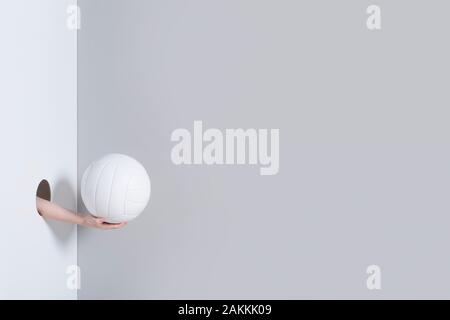 Hand in das Loch. Ein kind Hand hält eine weiße volleyball Ball auf grauem und weißem Hintergrund Stockfoto