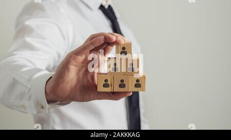 Business Executive holding Holzwürfel mit person Symbol auf sie bauen in einer Pyramide Struktur. Konzeptionelle Bild der Beschäftigung und der Humanressourcen. Stockfoto