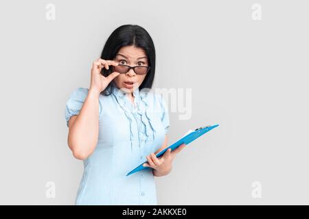 Freestyle. Asiatische Frau in Brillen auf Weiß mit Zwischenablage suchen Kamera isoliert stehende überrascht Stockfoto