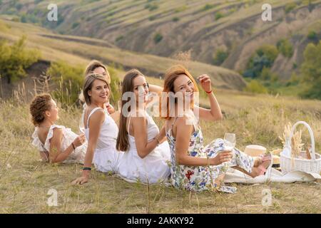 Die Firma fröhliche weibliche Freunde in weißen Kleidern mit Blick auf die grünen Hügel, entspannen Sie bei einem Picknick Stockfoto