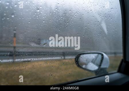 Regen fällt auf eine Seitenscheibe eines Autos Stockfoto
