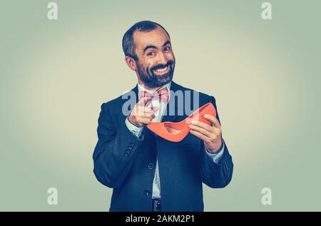 Große lächelnd, glücklich, bärtiger Mann mit einem roten hochhackigen Schuh in der Hand und zeigt mit dem Finger. Halbe Länge Körper. Eine einzige Person. Stockfoto