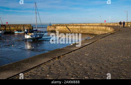 Geerdete Segelboote in Schlamm bei Ebbe mit langer gebogener Hafenmauer, Fisherrow Harbour, Musselburgh, Schottland, Großbritannien Stockfoto