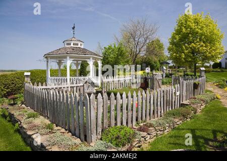 Gemüsegarten Grundstück durch die alten grauen verwittertes Holz- rustikalen Lattenzaun auf angehobenen Steinmauer mit gemischten mehrjährige Pflanzen im Garten im Hinterhof. Stockfoto