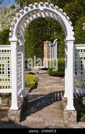 Flagstone Weg durch weiße hölzerne Gartenlaube, die zu formalen Garten mit Buxus sempervirens 'Green Gem' - Buchsbaum Hecken und Thuja occidentalis. Stockfoto