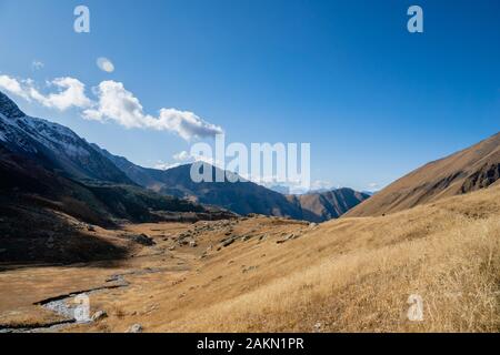 Huta Trekking Path Landschaft mit Fluss und Bergen im sonnigen Herbsttag - beliebte Trekking in den Kaukasusbergen, der Region Kazbegi, Georgien. Stockfoto