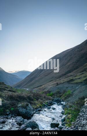 Die Landschaft der Ortschaft Juta mit Fluss und Bergen bei Sonnenuntergang - ein beliebter Trekkkingplatz in den Kaukasusbergen, der Region Kazbegi, Georgien. Stockfoto