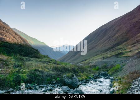 Die Landschaft der Ortschaft Juta mit Fluss und Bergen bei Sonnenuntergang - ein beliebter Trekkkingplatz in den Kaukasusbergen, der Region Kazbegi, Georgien. Stockfoto