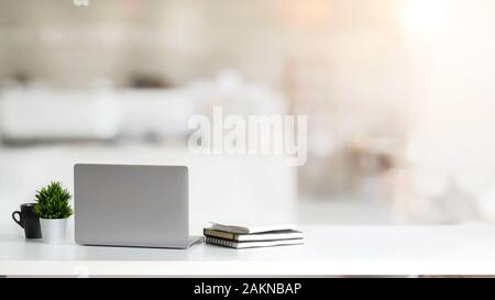 Nahaufnahme der einfachen Arbeitsbereich mit Laptop, Notebooks, Kaffee Tasse und Baum Topf auf weißen Tisch mit unscharfen Büro Hintergrund Stockfoto