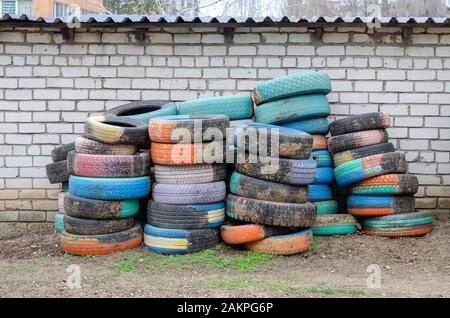 Reifen mit altem Auto lackiert. Viele bunte Reifen gegen eine weiße Ziegelwand. Draußen Ohne jeden Stockfoto