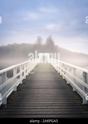 Alte Holzbrücke mit Dunsthitze und ruhiger Luft am Herbstmorgen in Finnland Stockfoto