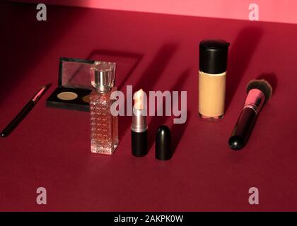 Frau flacher Schminkhintergrund mit dekorativen Kosmetika mit dunklen Schatten. Creme, Lippenstift, Parfüm, Mascara und Pinsel. Draufsicht auf den rosafarbenen Bac Stockfoto