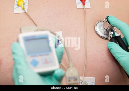 Die Hand des Arztes, der holter-herzmonitor auf die Brust eines jungen Mannes aufgibt Stockfoto