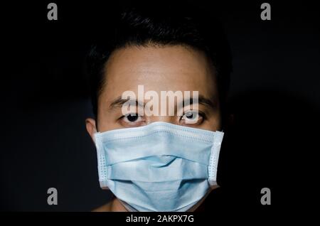 Nahaufnahme des jungen asiaten, der eine hygienische Maske mit dunklem schwarzen Untergrund trägt Stockfoto