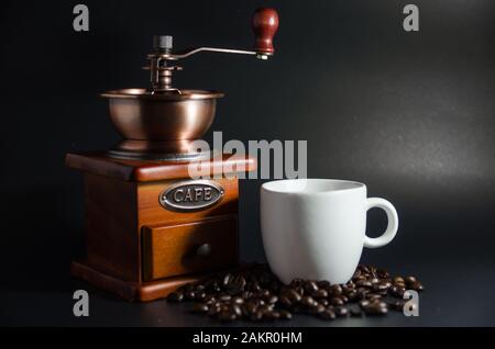 Weiße Kaffeetasse und Kaffeemühle und Kaffeebohnen auf schwarzem Hintergrund Stockfoto