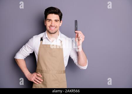 Portrait des positiven fröhlichen Friseursalons Mann Haltekamm bereit stylische Frisur tragen weißes Hemd isoliert über grauem Farbhintergrund Stockfoto