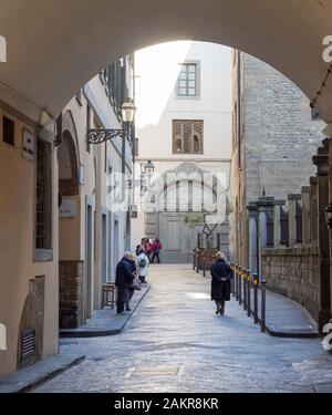 Florenz, Italien, 6. Januar 2020: Touristen und Einheimische in einer Seitenstraße von Florenz in der Toskana. Eindrucksvolle alte Tür hinter sich. Stockfoto