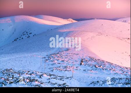 Winterberge Grat in rosa Sonnenaufgangsfarben, Hügel bedeckt von weißem Schnee. Stockfoto
