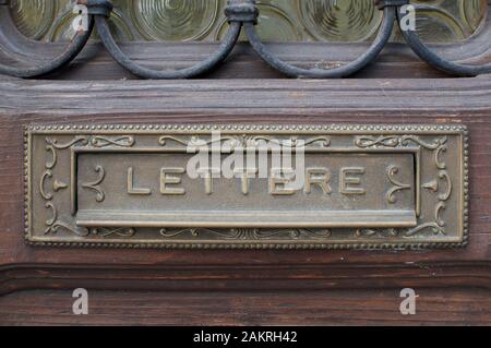 Blick auf einen alten Postkasten, der in eine Holztür mit der Aufschrift "Lettere" (bedeutet Buchstaben) integriert ist. Gefangen in einem typischen italienischen Dorf am See Stockfoto