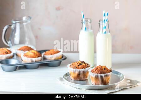 Vanillekaramel-Muffins in Papierbecher und Milchflaschen auf weißem Holzhintergrund. Köstlicher Cupcake. Hausgemachte Biskuitkuchen. Platz für Text kopieren. Stockfoto