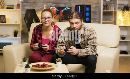 Vergrößern Sie die Aufnahme eines schönen jungen Paares, das Videospiele mit Controllern auf dem Sofa spielt. Stockfoto