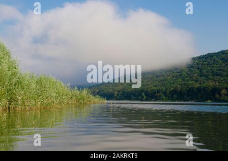 Morgennebel über den gespiegelten Gebirgsfluss vor dem Hintergrund von Bergen und blauem Himmel Stockfoto