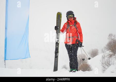 Freerider Woman Skier mit fetten/breiten Skiern, die neben einer leeren blauen Flagge stehen, während eines Whiteout-Tages im Skigebiet Les Sybelles, Frankreich. Stockfoto