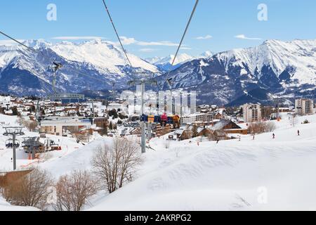 Les Sybelles, Frankreich - 14. März 2019: Bergdorf La Toussuire, von einem beweglichen Sessellift aus gesehen, in der Skidomäne Les Sybelles. Winterblick auf die Sonne Stockfoto