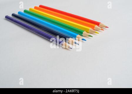 Satz von Regenbogenfarbenen Bleistiften auf leerem weißen Blatt, die zum Betrachter zeigen Stockfoto