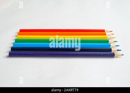 Satz von regenbogenfarbenen Bleistiften auf leerem Blatt weißem Papier, von der Seite aus gesehen Stockfoto