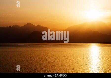 Golden Sun hinter jagged Misty Mountain Gebirge sichern einen glitzernden Mittelmeer in Antalya, Türkei Stockfoto